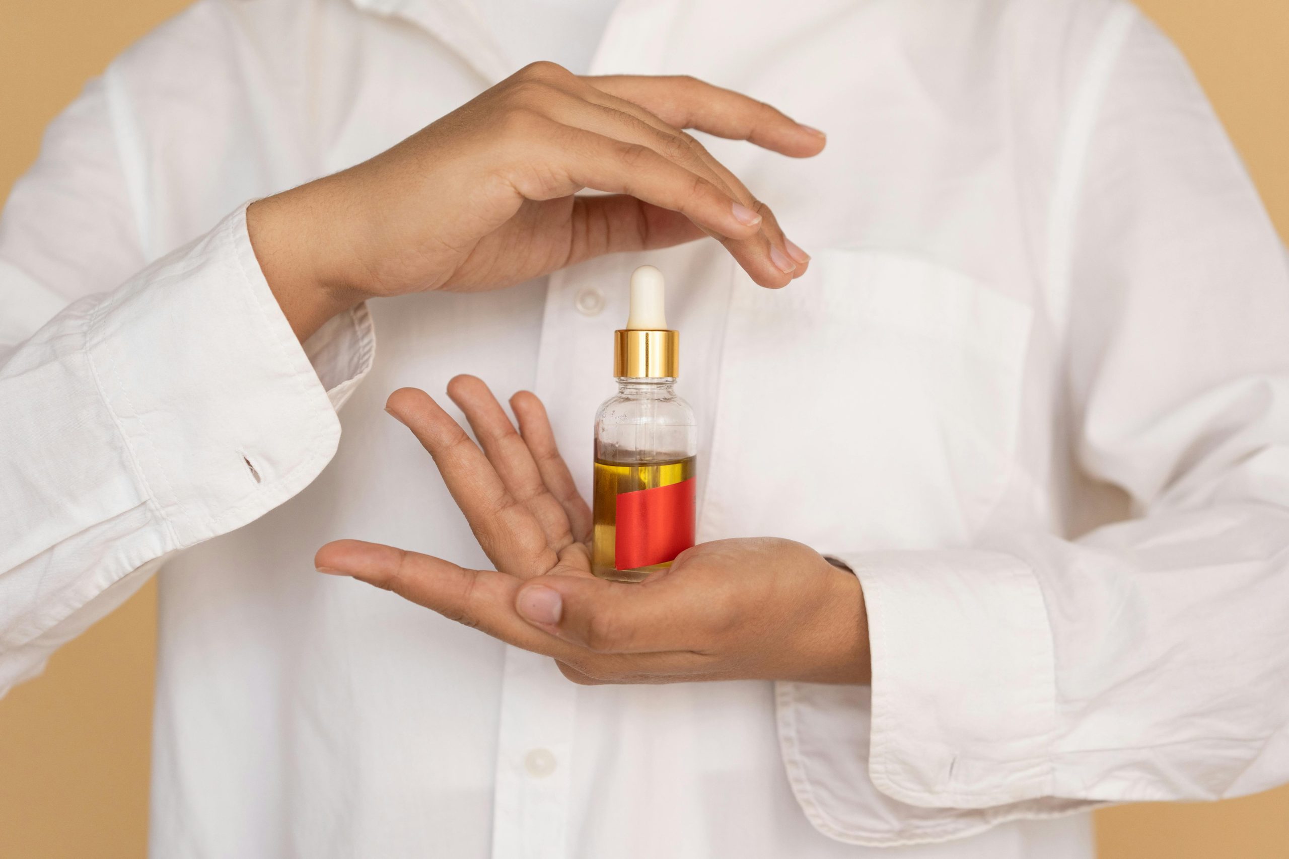 A person holding an essential oil bottle with a pipette against a neutral background. Skincare concept.
