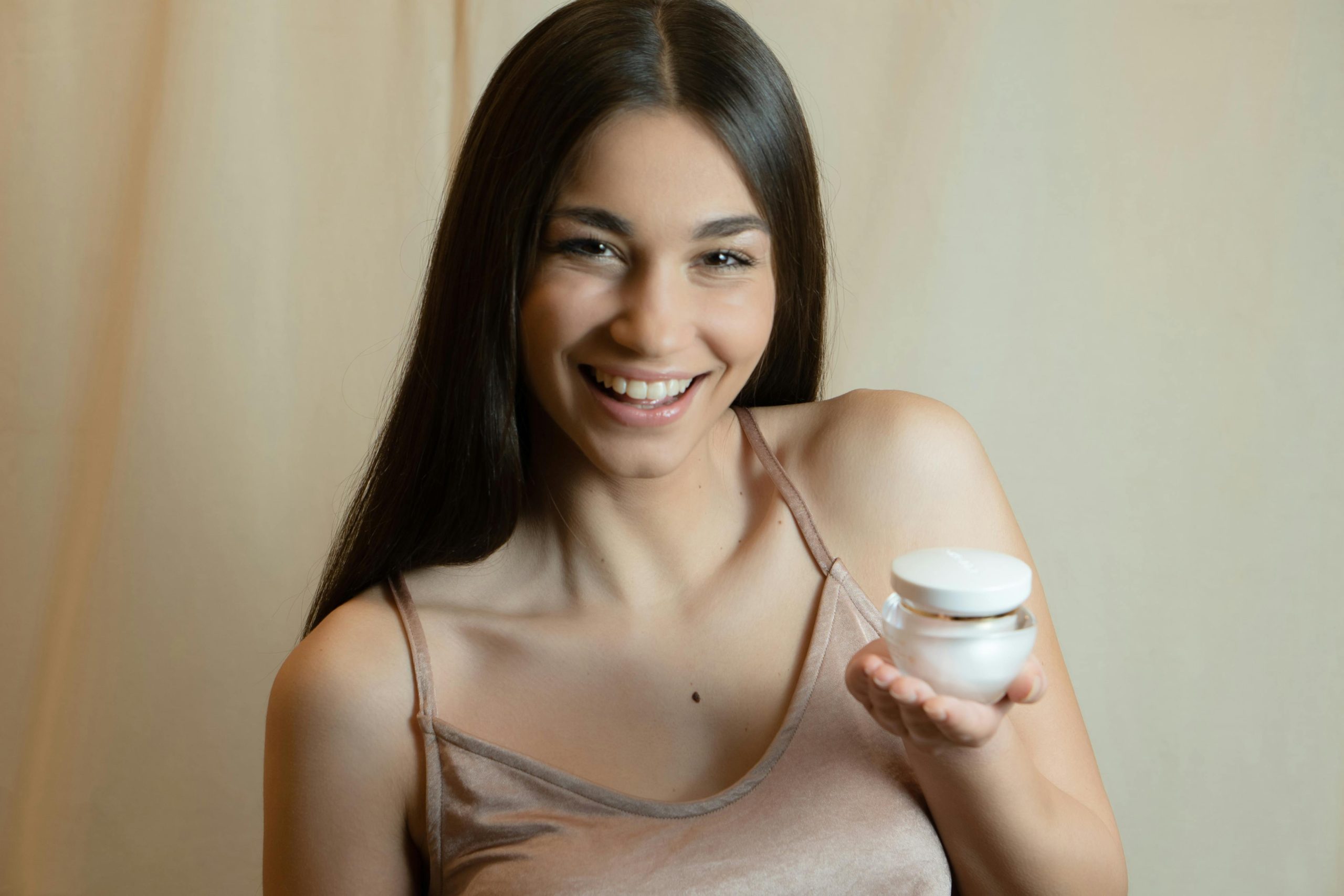 A smiling woman holding a skincare product, promoting beauty and wellness.